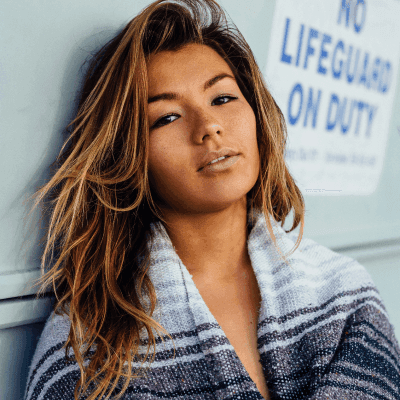 woman with black, white, and grey blanket leaning on wall with no lifeguard on duty signage