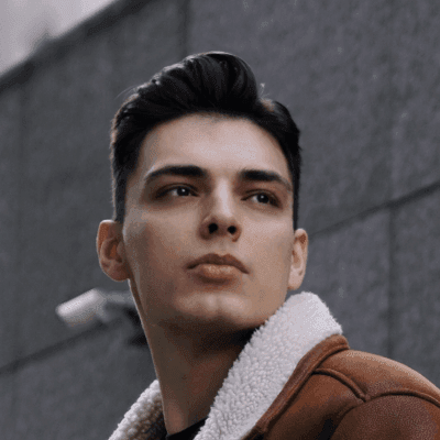 man in brown coat standing beside gray concrete wall during daytime